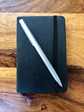 Laden Sie das Bild in den Galerie-Viewer, Slim silber X-Pen Drehkugelschreiber auf Moleskin